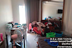 Clothes are scattered across the room, with a desk to one side being cluttered with papers and bottles of water.