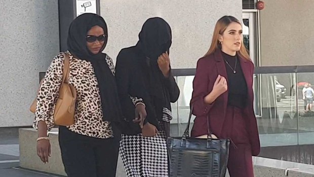 Diana Lasu leaves Brisbane Magistrates Court covering her face and linking arms with her mother.