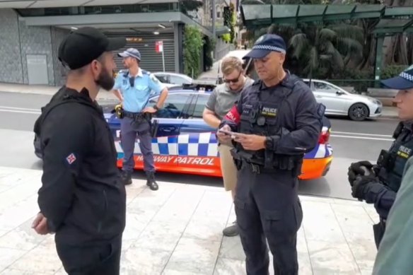 A NSW police officer serves Thomas Sewell (left) with an order prohibiting him from entering the City of Sydney on Australia Day.