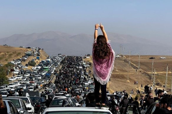 A girl with uncovered head stands atop a car during protests in Iran.