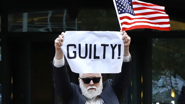 Protester Bill Christeson holds up a sign as the first count of guilty comes in for Paul Manafort.