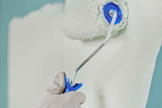 Woman painting blue wall white with paint roller during home renovation