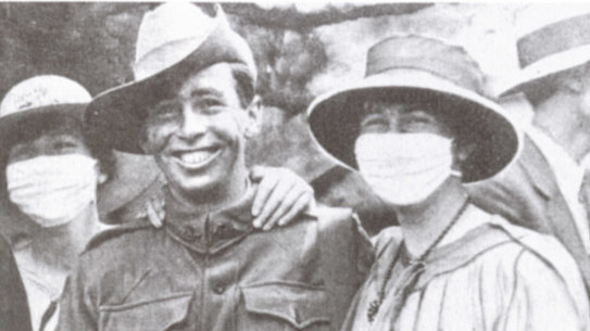A returned soldier poses with women in anti-flu masks, 1919.