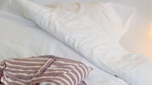 Striped pyjama shirt rests on a white bed with soft bedding and fairy lights in the background
