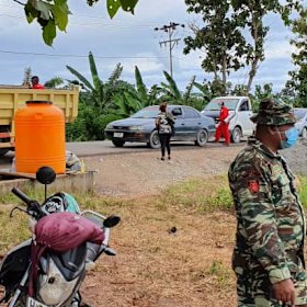 A road checkpoint in Baucau, Timor-Leste, where vehicles are sprayed inside and out, and a tank provides hand-washing water. 