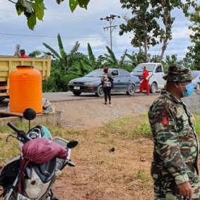 A road checkpoint in Baucau, Timor-Leste, where vehicles are sprayed inside and out, and a tank provides hand-washing water. 