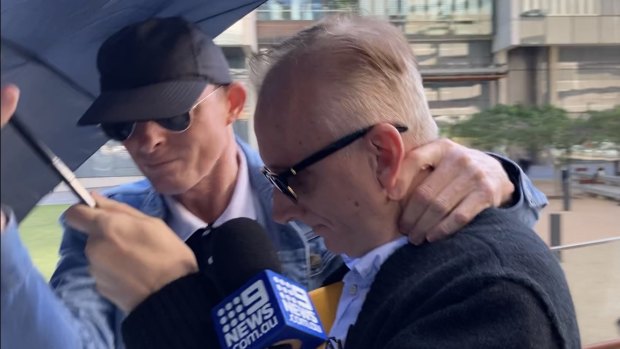 Neville William Gentry (right) leaves Brisbane Magistrates Court on Monday with his protective umbrella.