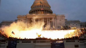 A flash lights up the front of the US Capitol as a mob of Trump supporters control the steps of the building.