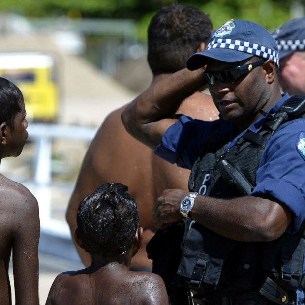 Children play on the main wharf on Palm Island while police officers patrol the island following riots in 2004.