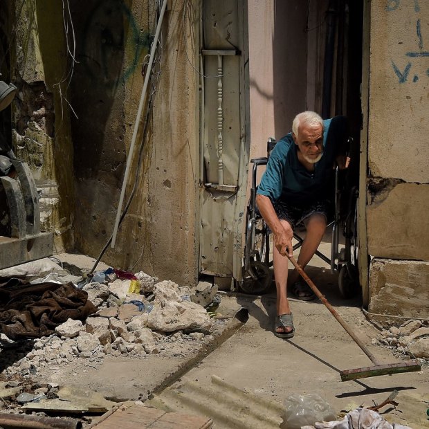 Abdulsalam Abdulqadir, 73, sweeps outside his gate from his wheelchair as an air strike hits nearby in West Mosul, Iraq, in October 2017.