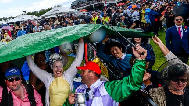 Racing crowds run for cover from a short rain burst at the 2016 Melbourne Cup. 