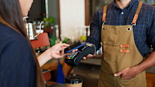 Male cafe employees various nationalities holding credit card acceptor QR code smiled. brunette female customer holding mobile phone scan payments holding disposable paper coffee cup small business.