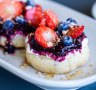 Golden sourdough crumpets with stewed fruit, strawberry slices, ricotta, honey and nuts. 