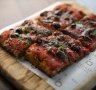 Puttanesca pizza a taglio is all crisp crust and salty, savoury topping of tomato sugo, anchovy, olives and basil.