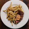 The bavette steak comes pink and glistening inside, and darkly crusty outside, smothered in skinny, skin-on fries.