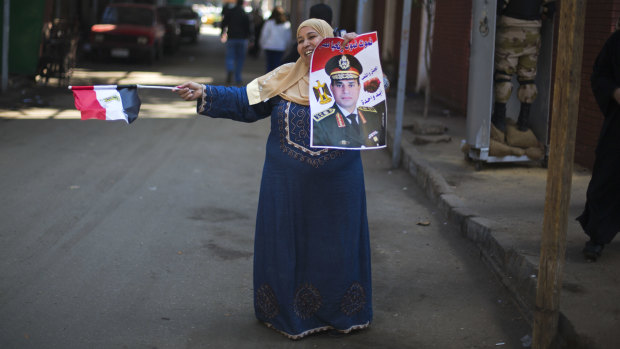 An Egyptian woman dances in front of a polling station holding a poster of Field Marshal Sisi.