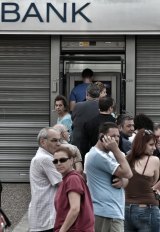 People stand in a queue to use ATM machines to withdraw cash at a bank in Athens.