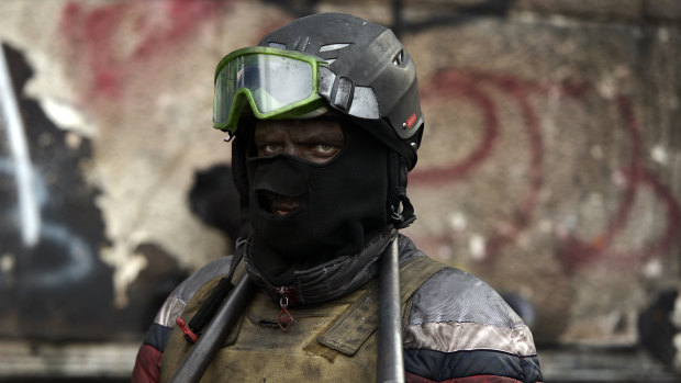 A masked Ukrainian anti-government protester stands at a roadblock in Kiev .