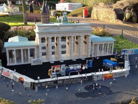 Tiny figures clamber atop a model of the Berlin Wall, built in front of a replica Brandenburg Gate.