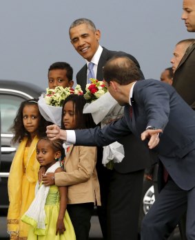 An aide directs children to look at cameras after they presented Barack Obama with flowers at Bole International Airport in Ethiopia.