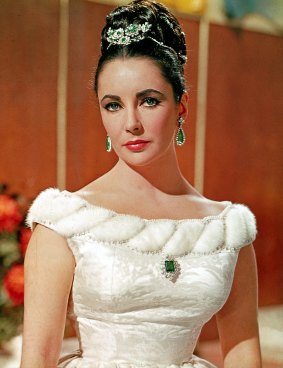 Elizabeth Taylor in a publicity photograph for the 1963 movie <i>The V.I.P.s</i> wearing her Bulgari platinum, emerald and diamond tremblant brooch and Colombian emerald brooch with earrings.