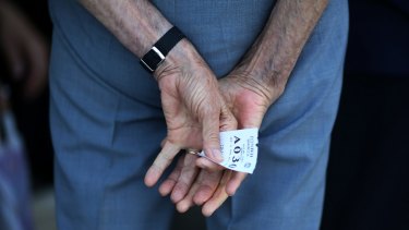 A pensioner holds a ticket as he waits his turn to be allowed inside the National Bank of Greece.