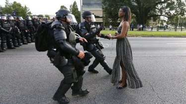 Police officers in riot gear face a woman in a dress during a Black Lives Matter protest in Baton Rouge.