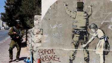 An Israeli soldier walks past a Banksy mural in Bethlehem. 