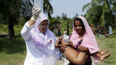 An Indonesian paramedic holds an IV drip while assisting a Rohingya mother.