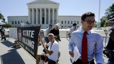 A news assistant runs past anti-death penalty demonstrators to his co-workers with copies of court decisions in front of the US Supreme Court building in Washington on Monday.