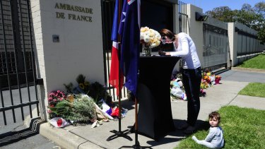 Kamara Buchanan, of Fisher, with her daughter Sophie, seven months, writes a message in a condolence book outside the embassy of France. 