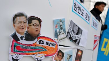 A South Korean protester holds a sign with pictures of President Moon Jae-in, left, and North Korean leader Kim Jong-un, second left, during a rally to denounce the US policy against North Korea and demand a peaceful Winter Olympics.