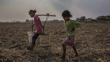 Ma Moe Thu, 11, and Zin Mar Win, 7, carry buckets of clean water across dry rice paddy fields back in Dala, a township south of Yangon, Burma. 