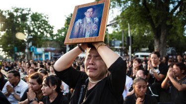 A Thai woman cries as she holds a picture of the late King Bhumibol Adulyadej  as people pay last respects to a passing van carrying the body of their king in Bangkok in October.