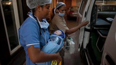 A newborn baby is transferred to an ambulance from a clinic in Anand, India, which has also banned surrogacy services for foreigners.