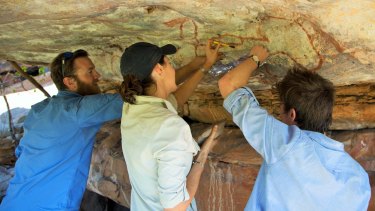 Researchers Nick Sundblom, Helen Green and Jordy Grinpukel remove tiny mineral accretions from a rock art panel motif in the Kimberley. Courtesy of Kimberley Foundation Australia.
