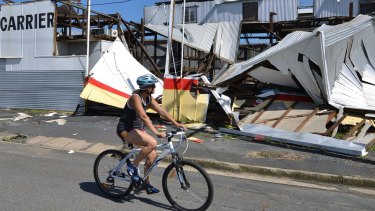 A resident rides past a cyclone damaged business in Rockhampton.