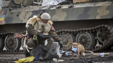 A Russia-backed rebel, with his feet on Ukraine's flag, watches a small dog holding a can of food in Debaltseve, Ukraine, on Friday.