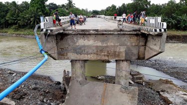 People gather on a bridge damaged by the onslaught of the flooding brought about by tropical storm Tembin.