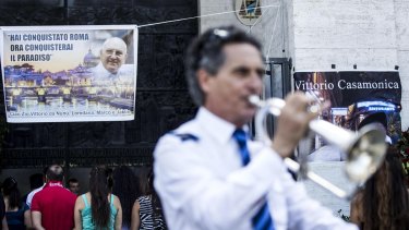 A man plays a trumpet as a banner showing purported Mafia boss Vittorio Casamonica reading "You conquered Rome, now you'll conquer paradise," hangs from the facade of the Don Bosco church.