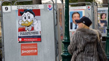 A woman looks at a poster with the Disney character Uncle Scrooge fixed over the official poster of French presidential election candidate for the far-left coalition "La France insoumise" Jean-Luc Melenchon.