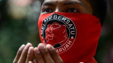 A pro-government 'red shirt' protestor prays with a face mask which reads read " Malay United" on the face, at a pro-government demonstration in Kuala Lumpur this month. 