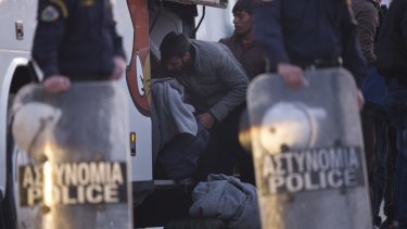 Migrants take their belongings from a bus before boarding a ferry for Turkey as riot police watch on Monday.