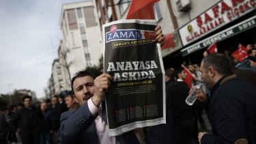 A man holds Saturday's copy of the newspaper which reads "the constitution suspended" as people gathered in support outside the headquarters of Zaman newspaper in Istanbul, on Sunday. 