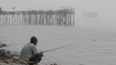 A man fishes near a wooden jetty shrouded in haze in Port Klang, outside Kuala Lumpur, Malaysia.