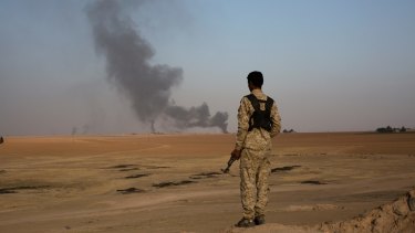 A member of an Arab tribal militia fighting the Islamic State group watches as smoke rises from a crude oil refinery in Syria.