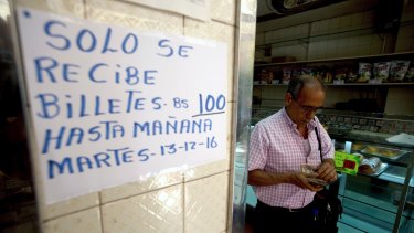 A man counts his 100-bolivar notes next to a sign on a bakery wall alerting customers that 100-bolivar notes will only be accepted until Tuesday,  December 13.