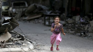 A girl runs near damaged buildings and debris in Jobar on Wednesday.