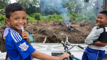 Children ride their bicycles in Pelalawan, in Riau province as small fires burn in the background. 