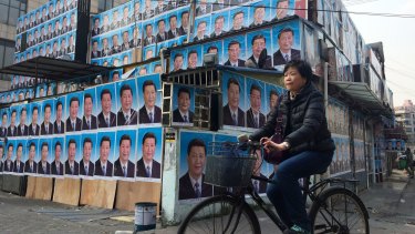 A woman cycles past a building covered in portraits of Chinese President Xi Jinping in Shanghai.